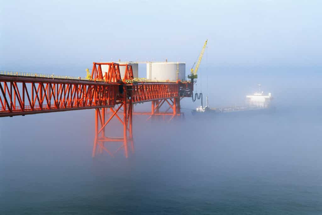 A large metal structure that has been coated by Corrocoat products and is reaching out to an offshore site that is surrounded by fog