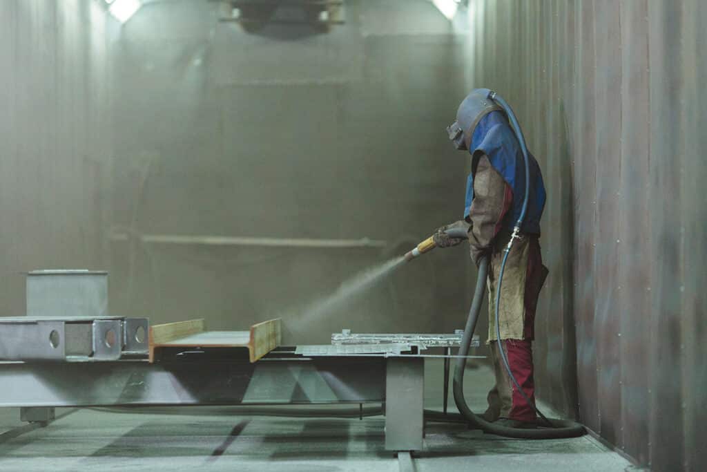 An employee prepares a metal part for painting